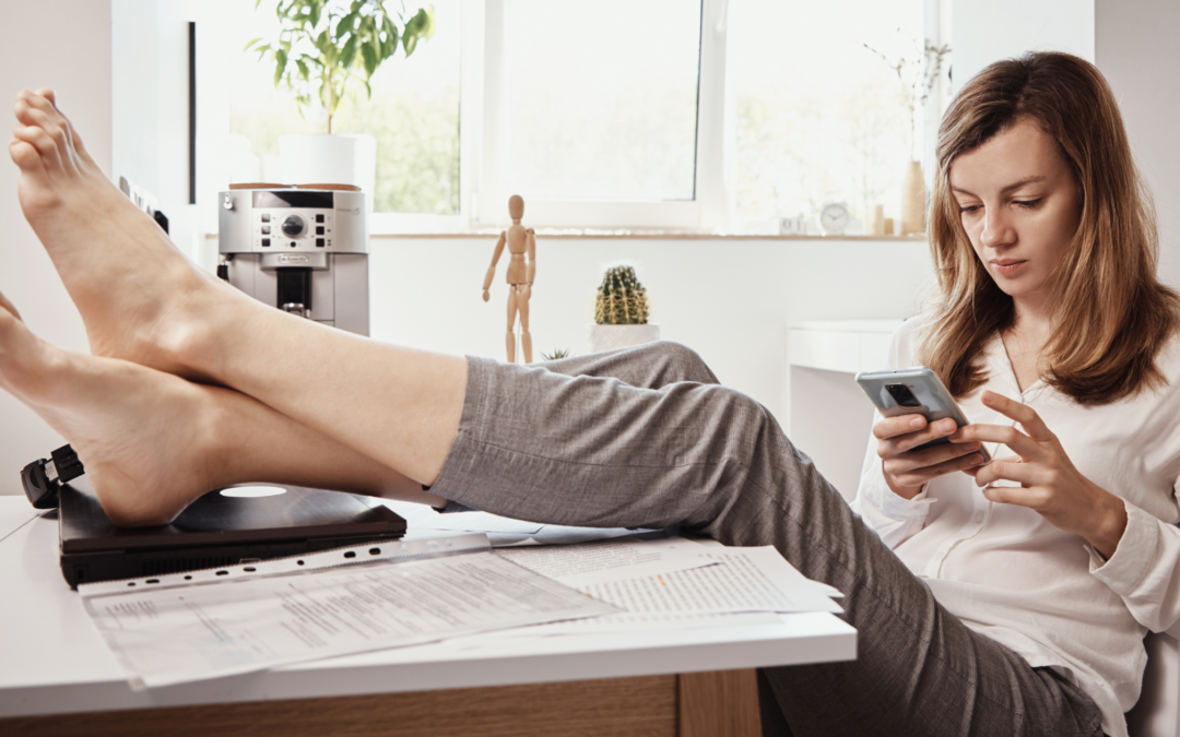 woman with feet on desk scrolling through phone